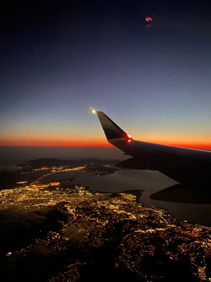 the wing of an airplane as it flies over a city at night with lights on