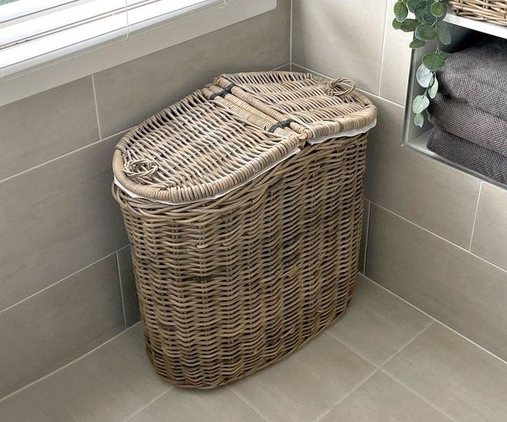 a wicker laundry basket sitting next to a window in a white tiled bath room