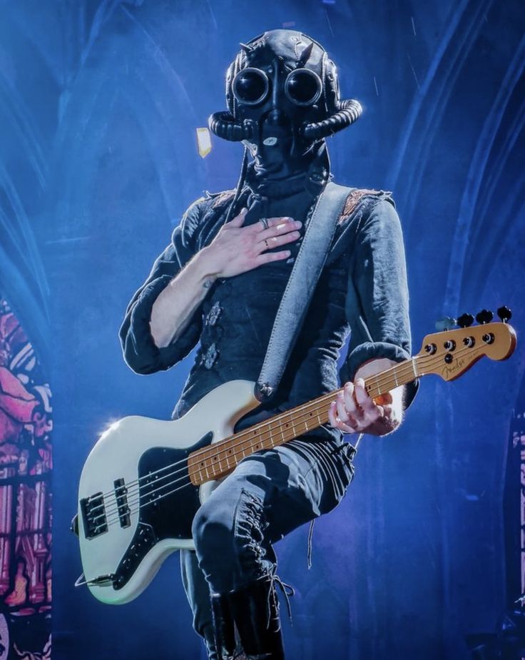 a man wearing a gas mask and holding a guitar in front of him on stage