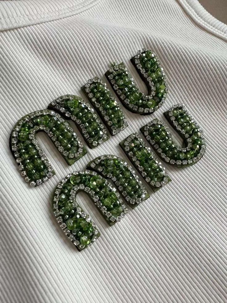 the letters and numbers are made out of green beads on top of a white t - shirt