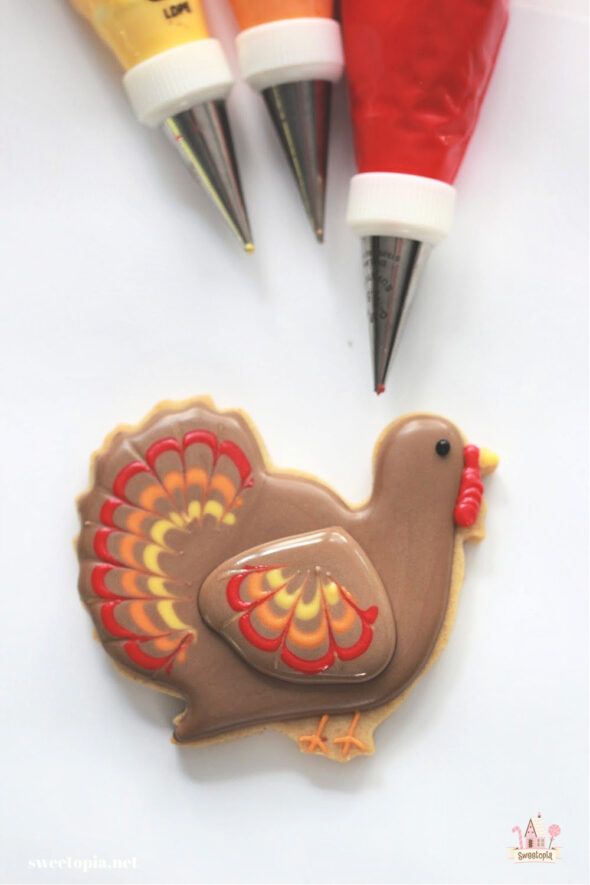 three crayon markers are next to a decorated cookie with a turkey on it