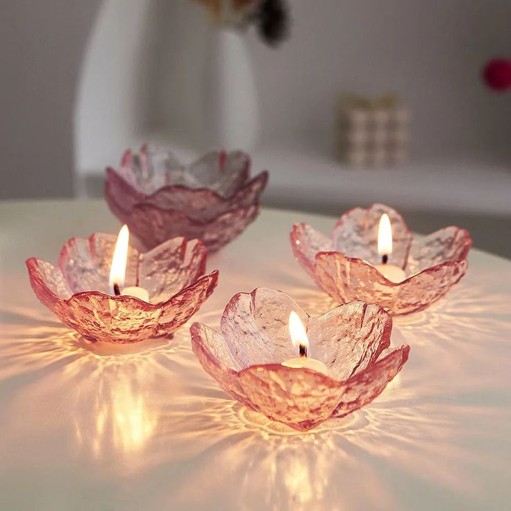 three pink glass candles sitting on top of a white table next to a vase with flowers in it