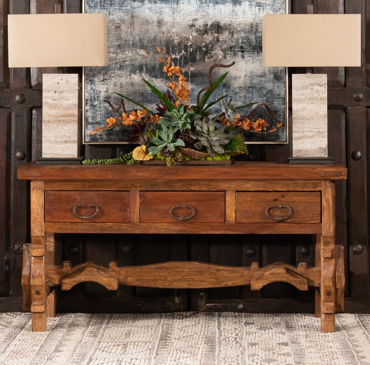 an old wooden table with flowers on it and a painting in the backround