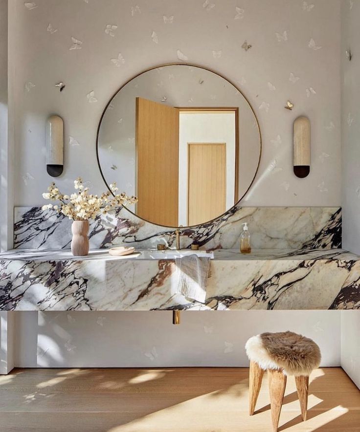 a bathroom with marble counter tops and stools in front of a round mirror on the wall