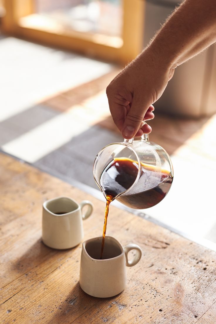 a person pours coffee into two cups