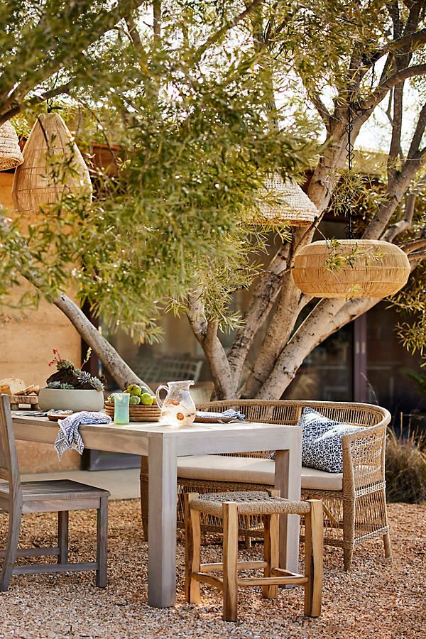 an outdoor dining table with four chairs and two hanging baskets on the tree's branches