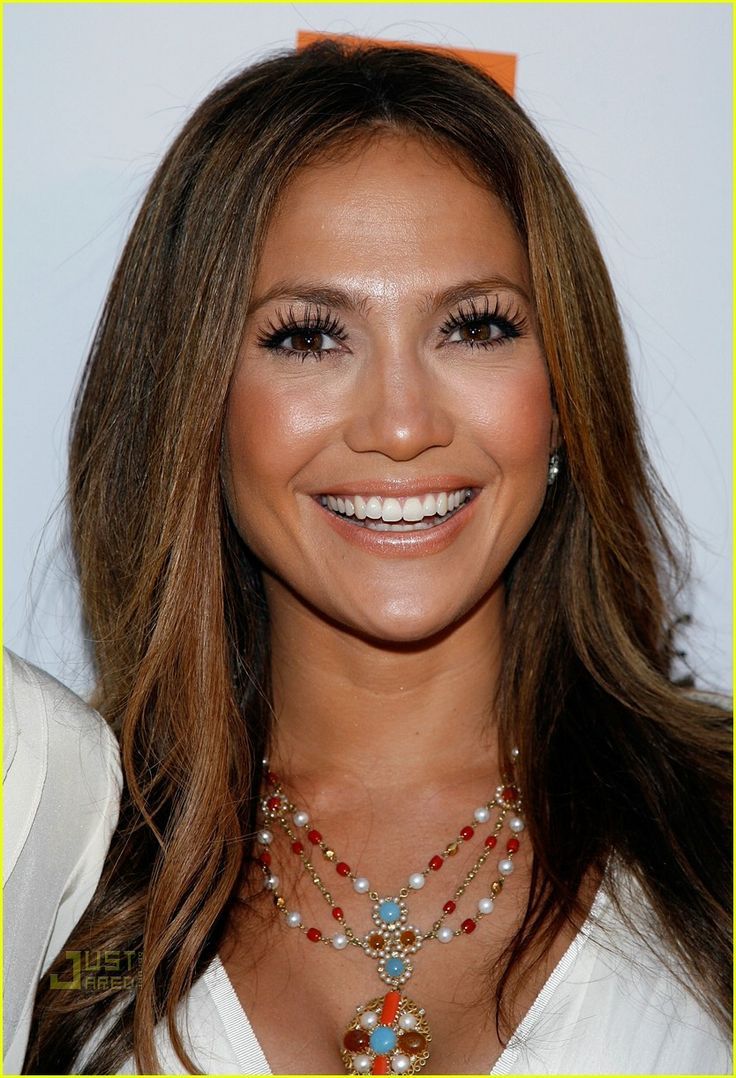 a woman with long hair and pearls on her necklace smiles at the camera while standing in front of a white backdrop