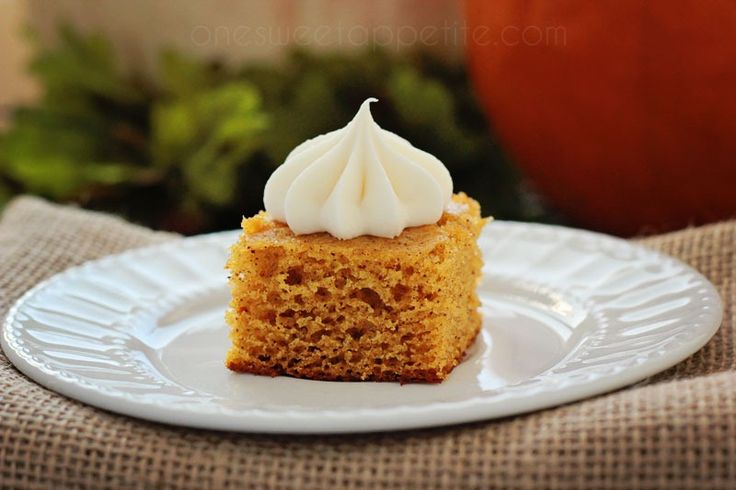 a piece of cake on a white plate with frosting and pumpkins in the background