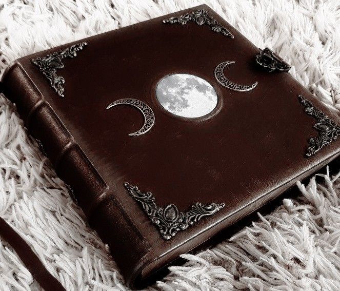 a brown leather book sitting on top of a white rug with the moon in the middle