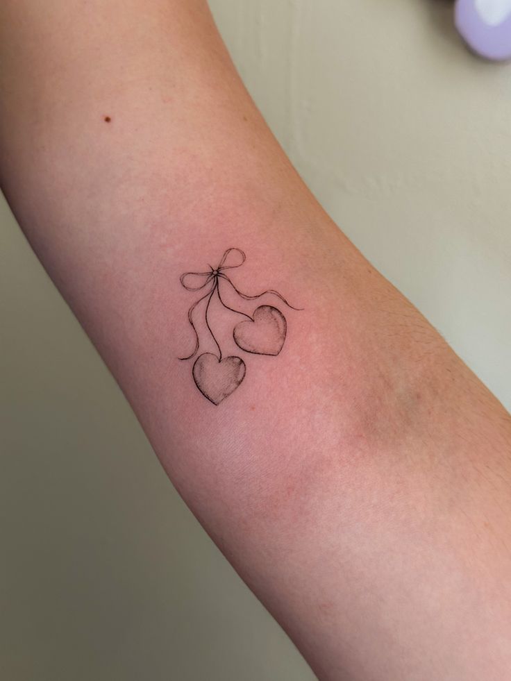 a tattoo on the arm of a woman with three hearts and a ribbon attached to it