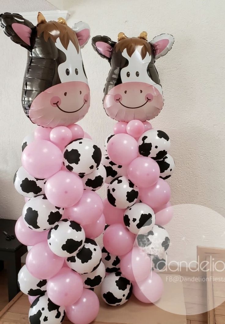 two balloons shaped like cows with faces on them are standing next to each other in front of a wall