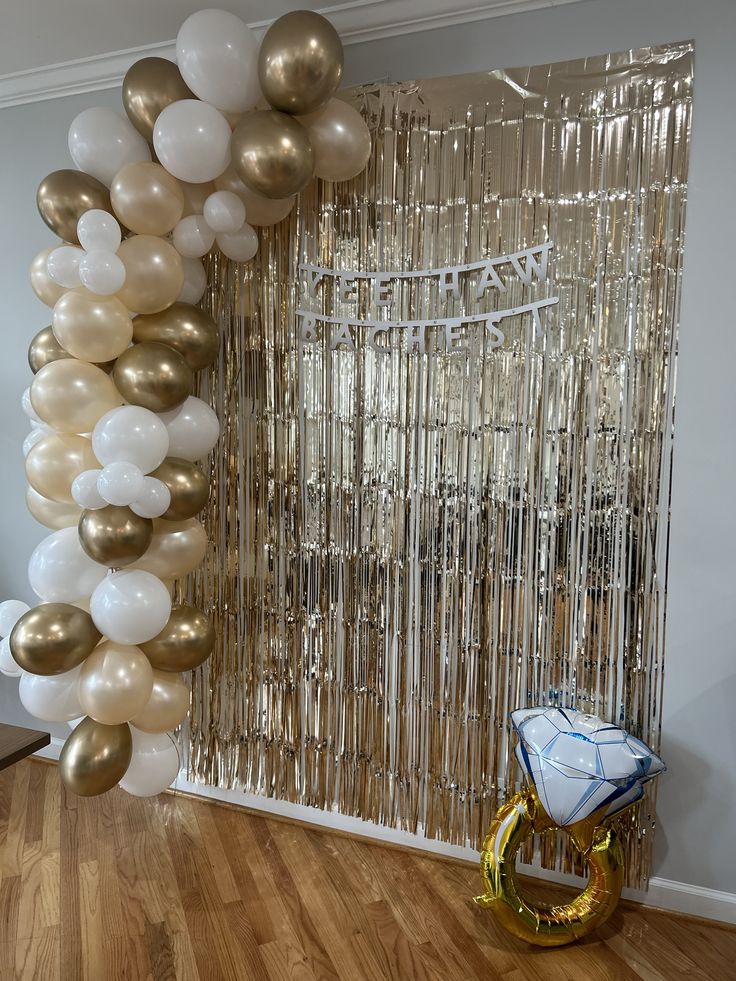 balloons and streamers are hanging in front of a backdrop made of gold, white and silver confetti