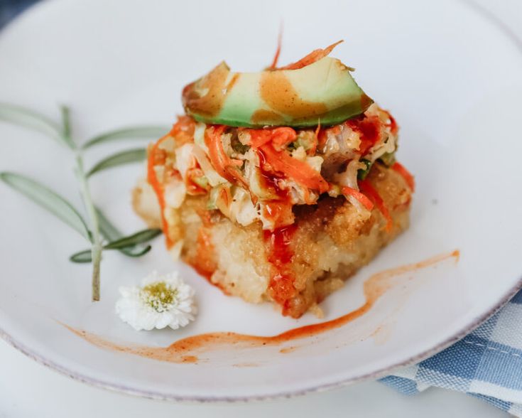 a piece of food on a white plate with sauce and green leafy garnish