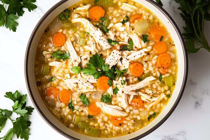 a bowl of chicken and barley soup with carrots, parsley and parsley