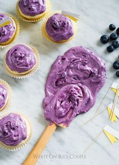 blueberry cupcakes with purple frosting on a marble counter top next to other cupcakes