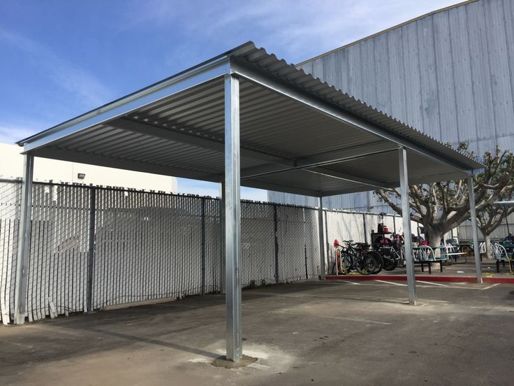 an outdoor covered parking lot with motorcycles parked in the background and a building behind it