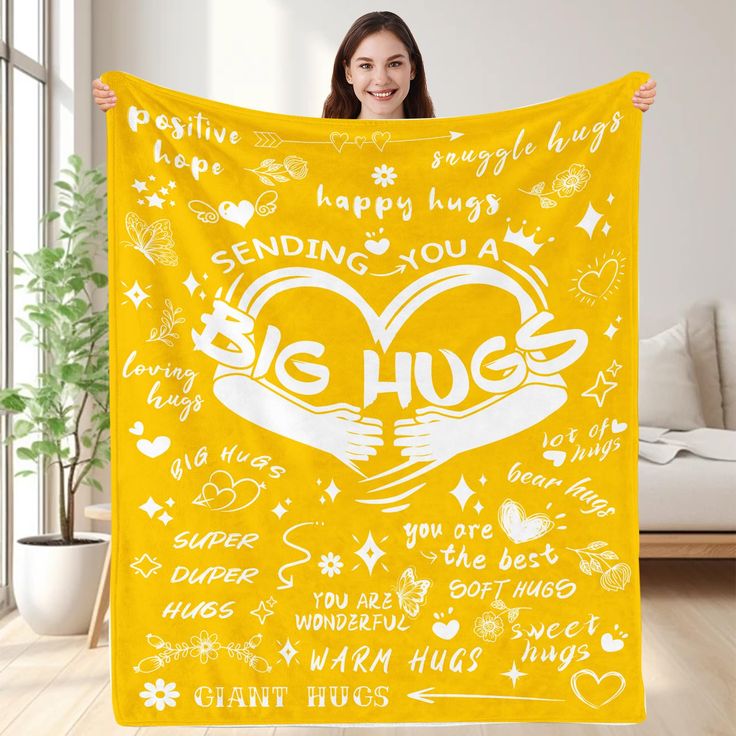 a woman holding up a yellow blanket that says, sending you a big hug