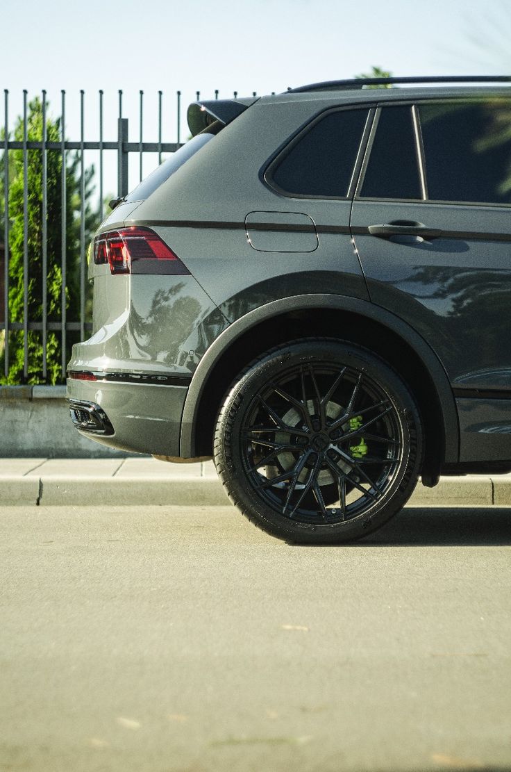 an suv parked on the side of the road near a fence and bushes in front of it