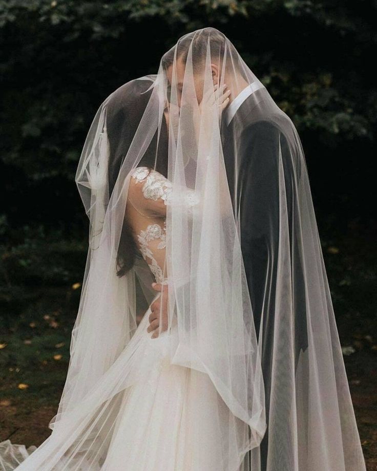 a bride and groom kissing in front of some trees with their veils pulled back