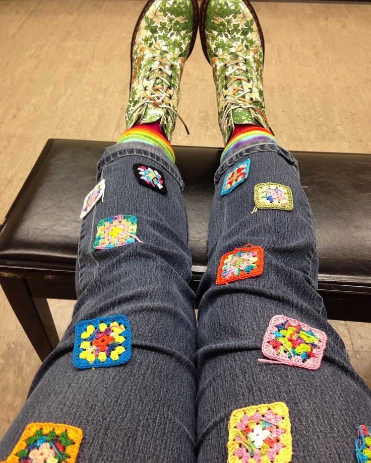 the legs and feet of a person wearing jeans with colorful patches on them, sitting in front of a black bench