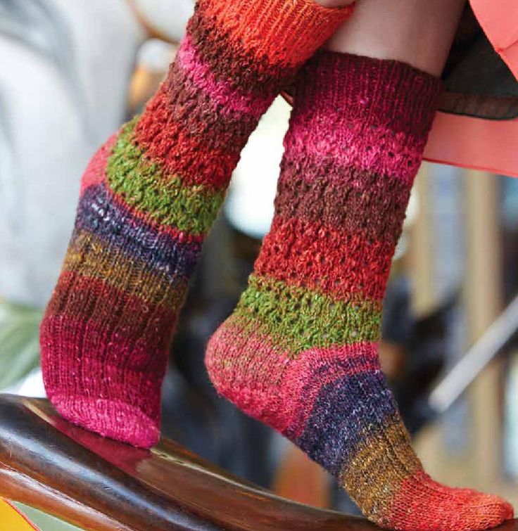 a woman's legs in colorful socks sitting on top of a wooden chair with her feet up