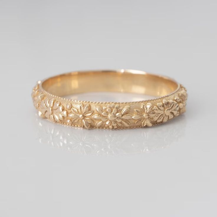 a gold wedding band with flowers on the side and an intricate design in the middle