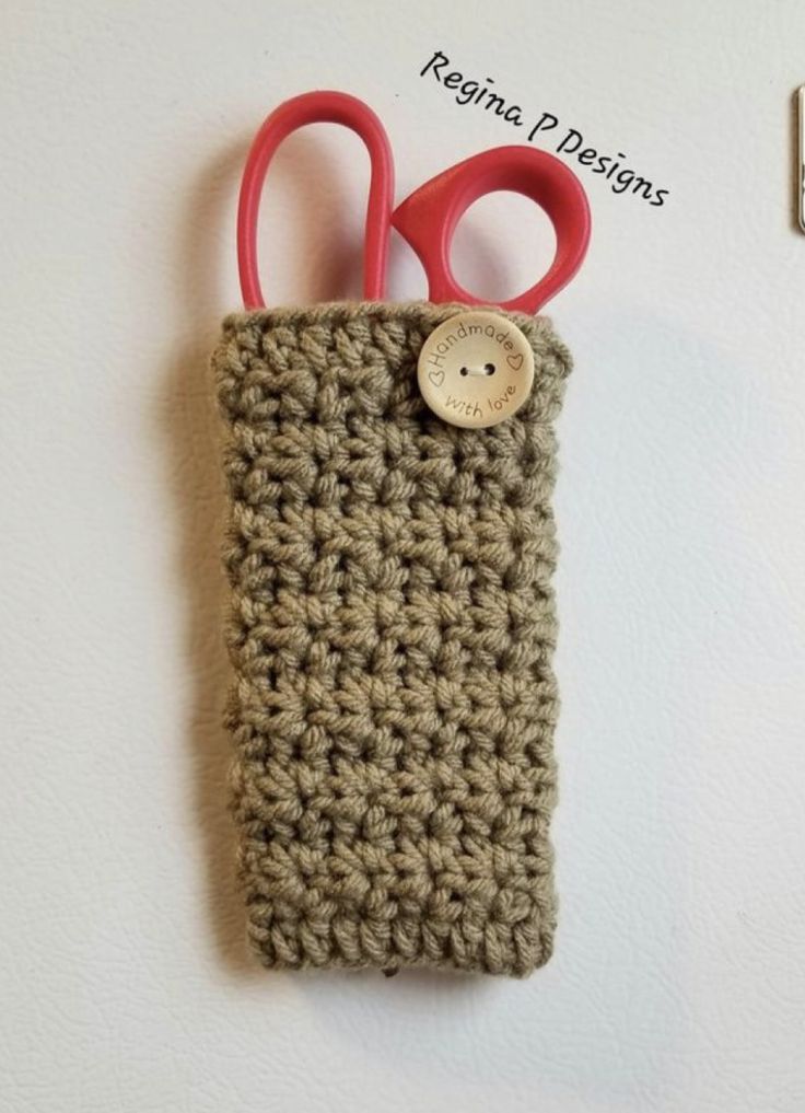 a crocheted case with scissors and a button on the front is attached to a hook