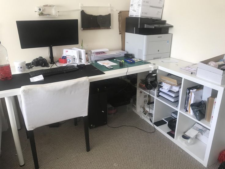 a desk with two computer monitors and a printer on it in an office space next to a bookshelf