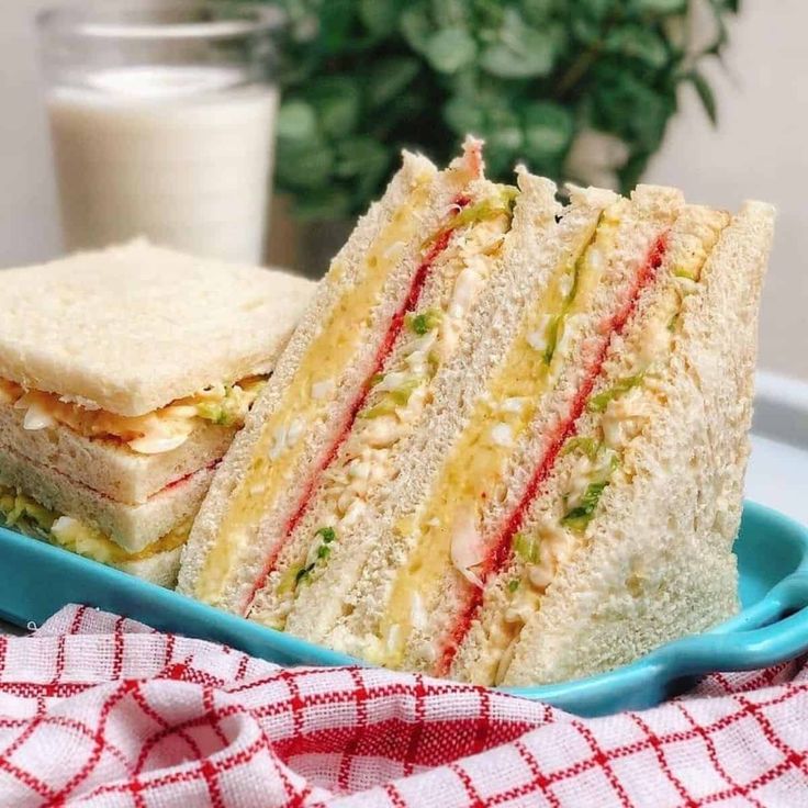 two sandwiches on a blue plate next to a glass of milk and a red checkered napkin