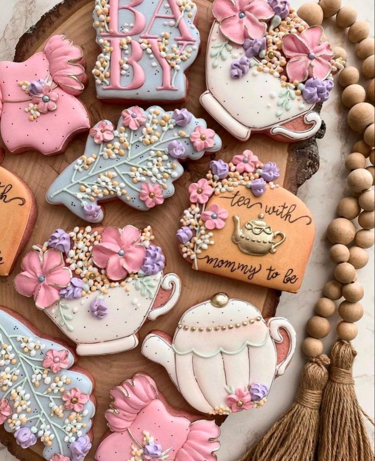 baby shower cookies are arranged on a wooden platter with tassels and beads