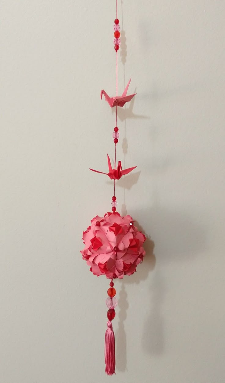 pink paper flowers and birds hanging from a string on a white wall with red beads