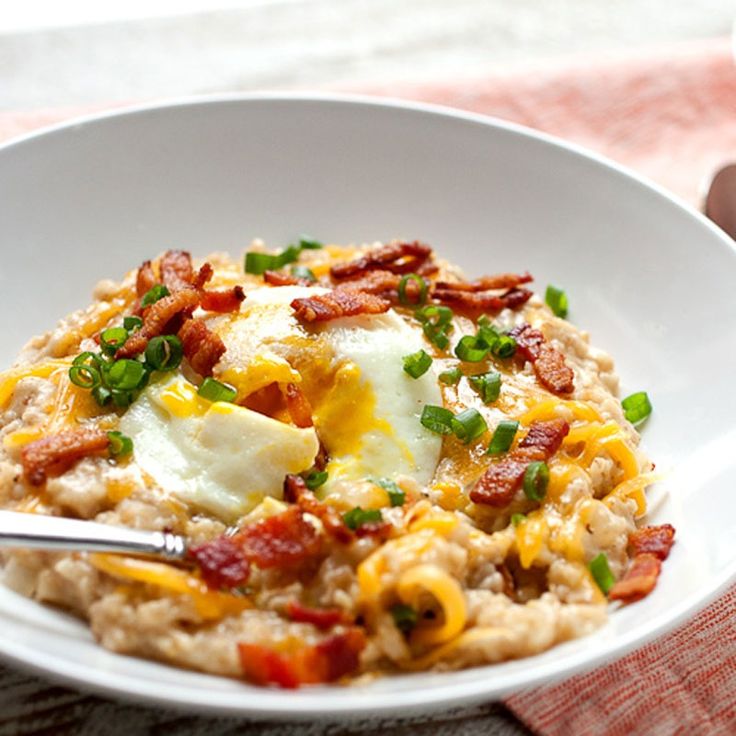 a white bowl filled with oatmeal topped with bacon and an egg on top