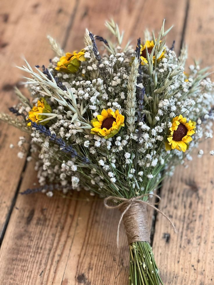 a bouquet of sunflowers and baby's breath on a wooden table with twine