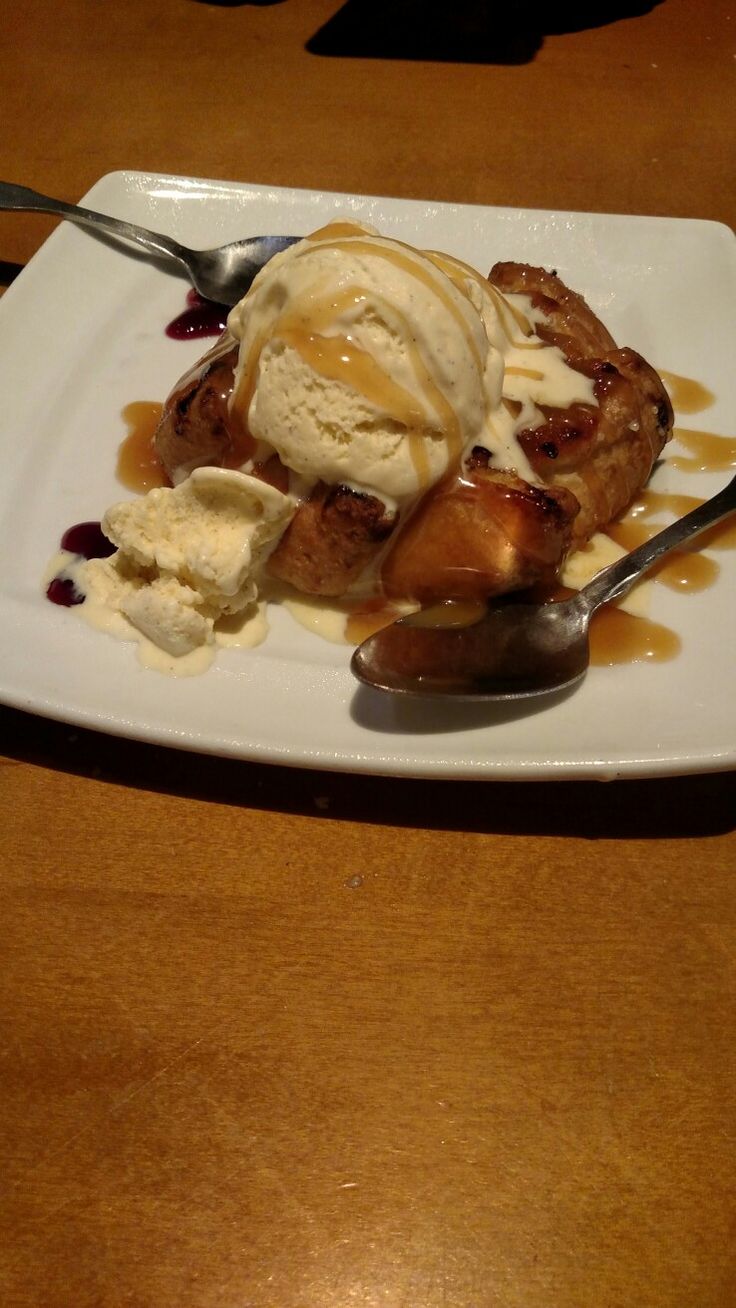 a white plate topped with dessert and ice cream on top of a wooden table next to a fork