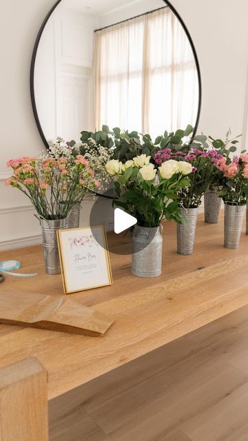 flowers are arranged in vases on a wooden table with a mirror above the table