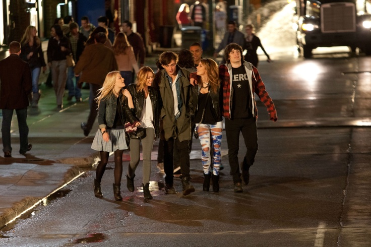 a group of young people walking down the street at night in front of a bus