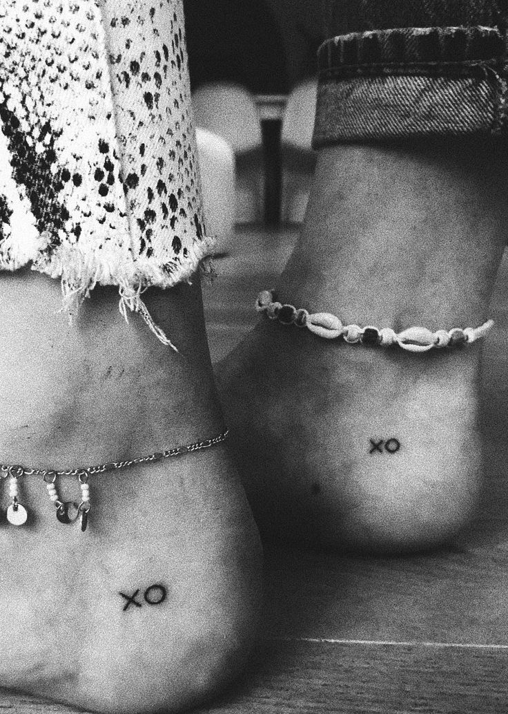 black and white photograph of two feet with tattoos on their ankles, one has the word x