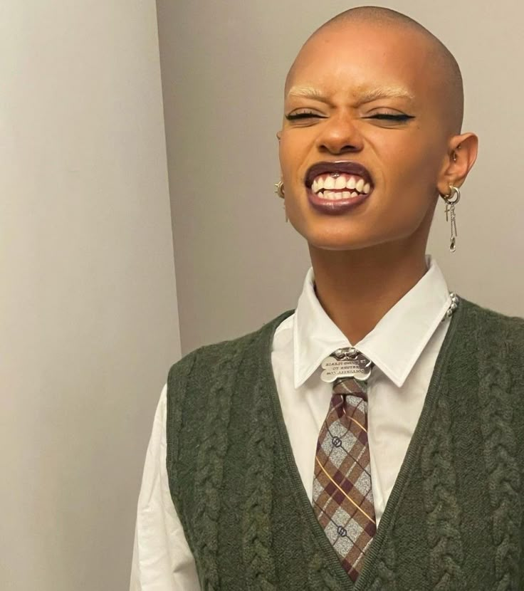 a bald headed man wearing a vest and tie with his mouth open in front of the camera