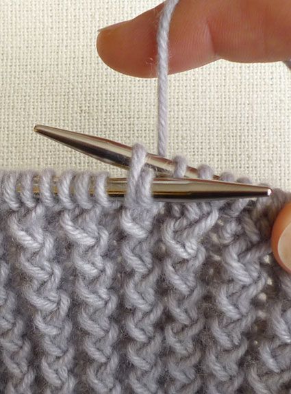 a hand holding a crochet hook over a knitted object