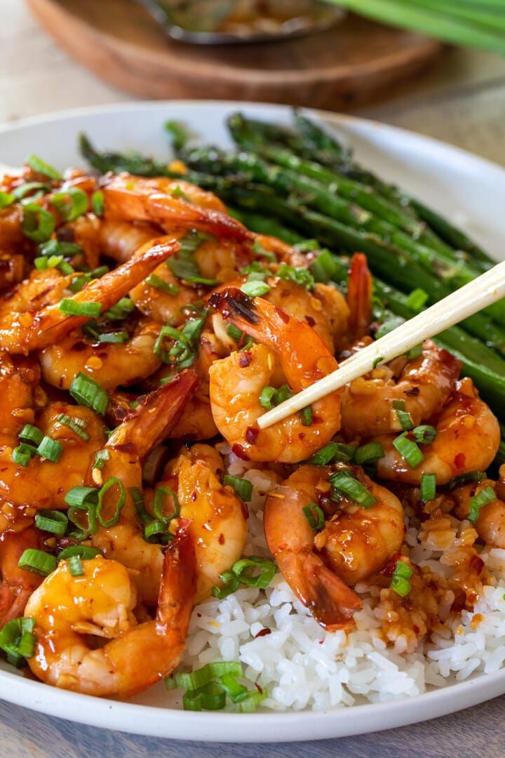 a white plate topped with rice and shrimp next to asparagus covered in sauce