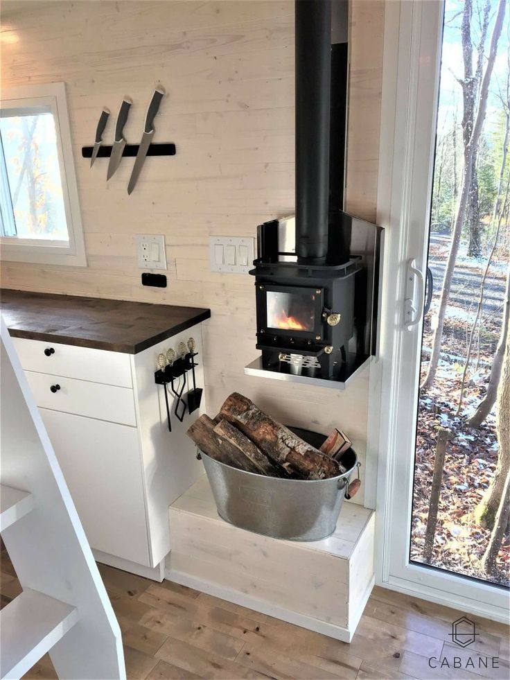 a stove in the corner of a room next to a counter and window with a bucket full of firewood