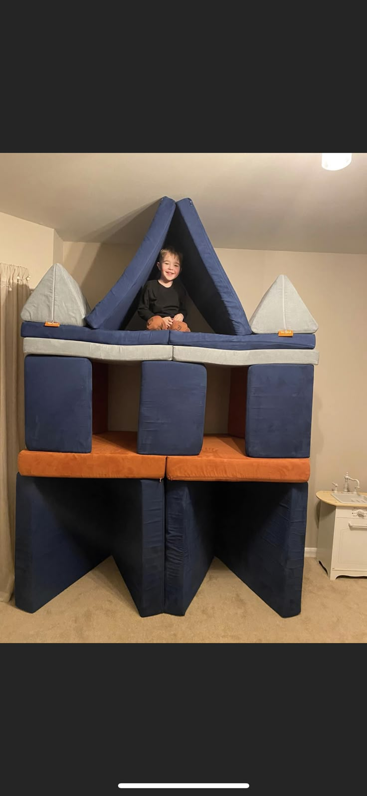 a child is sitting in a blue and orange castle bed that has been built into the wall