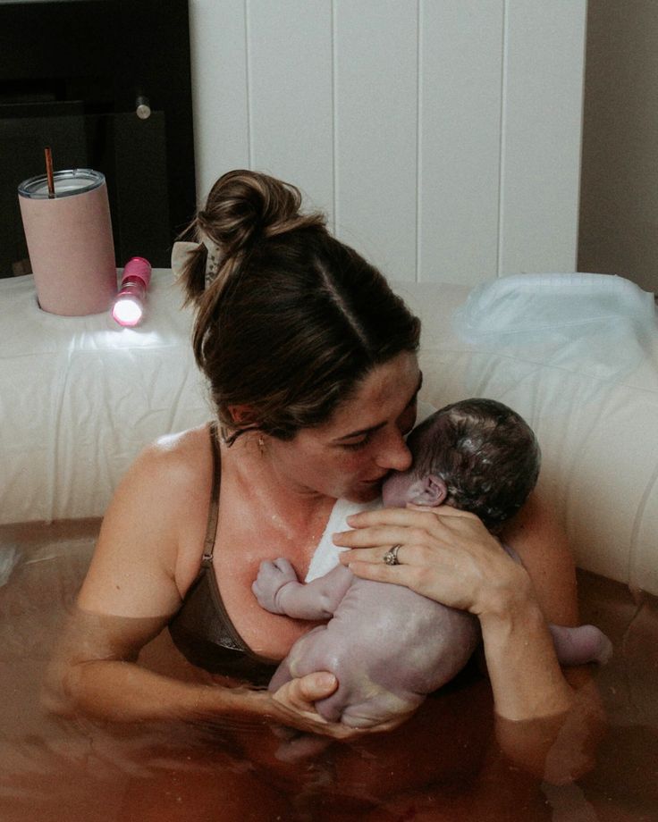 a woman holding a baby in a bathtub while she is breastfeeding it