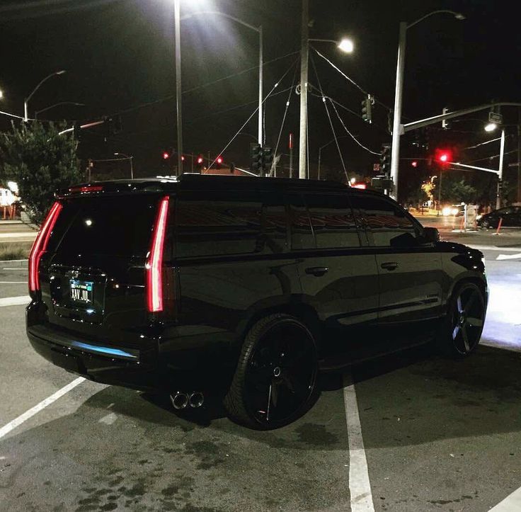 a black suv parked in a parking lot at night with street lights on the side