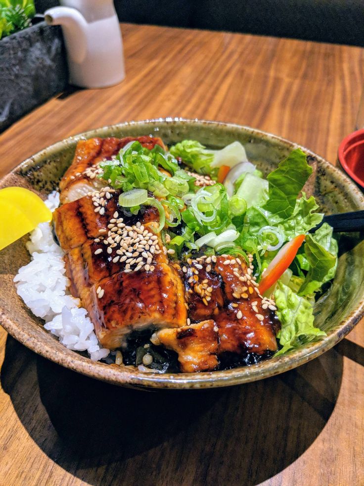 a bowl filled with meat and rice on top of a wooden table