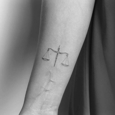 a woman's arm with a tattoo on it that has a scale and arrow