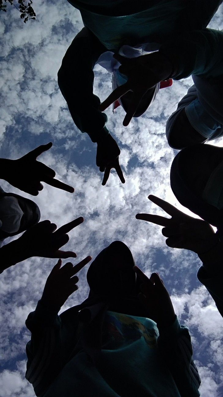 several people standing in a circle with their hands pointing at the sky and clouds behind them