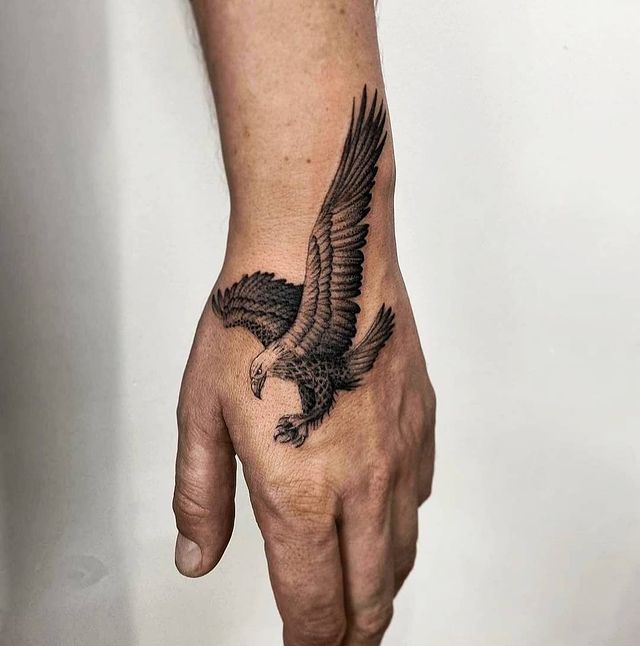 an eagle tattoo on the left hand is shown in black and grey ink, with its wings spread out