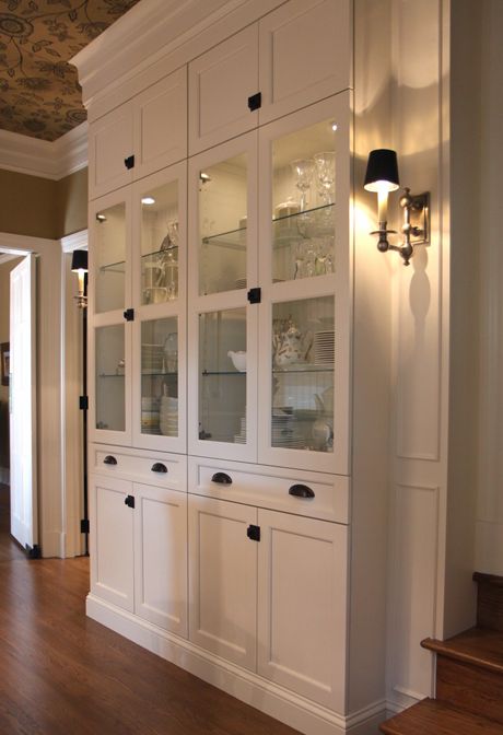 a white china cabinet with glass doors in the middle of a living room and stairs leading up to it