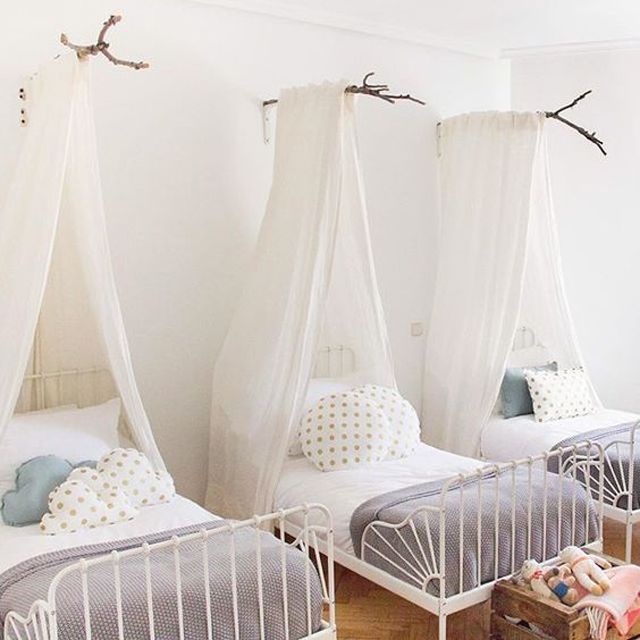 two twin beds with mosquito netting over them in a white walled room, one is made up as a canopy and the other has pillows on it